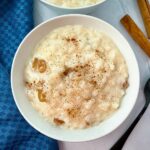 rice pudding in a white bowl with cinnamon sticks and black spoon on the side