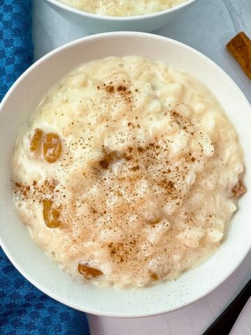 rice pudding in a white bowl with cinnamon sticks and black spoon on the side