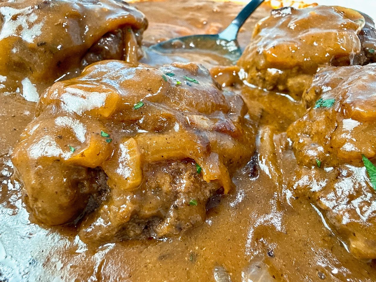 hamburger steaks and gravy with a black serving spoon