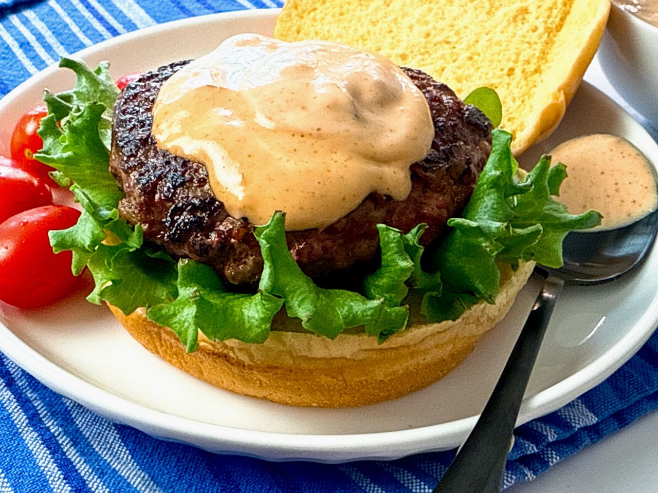 burger on a bun with lettuce and spicy sauce