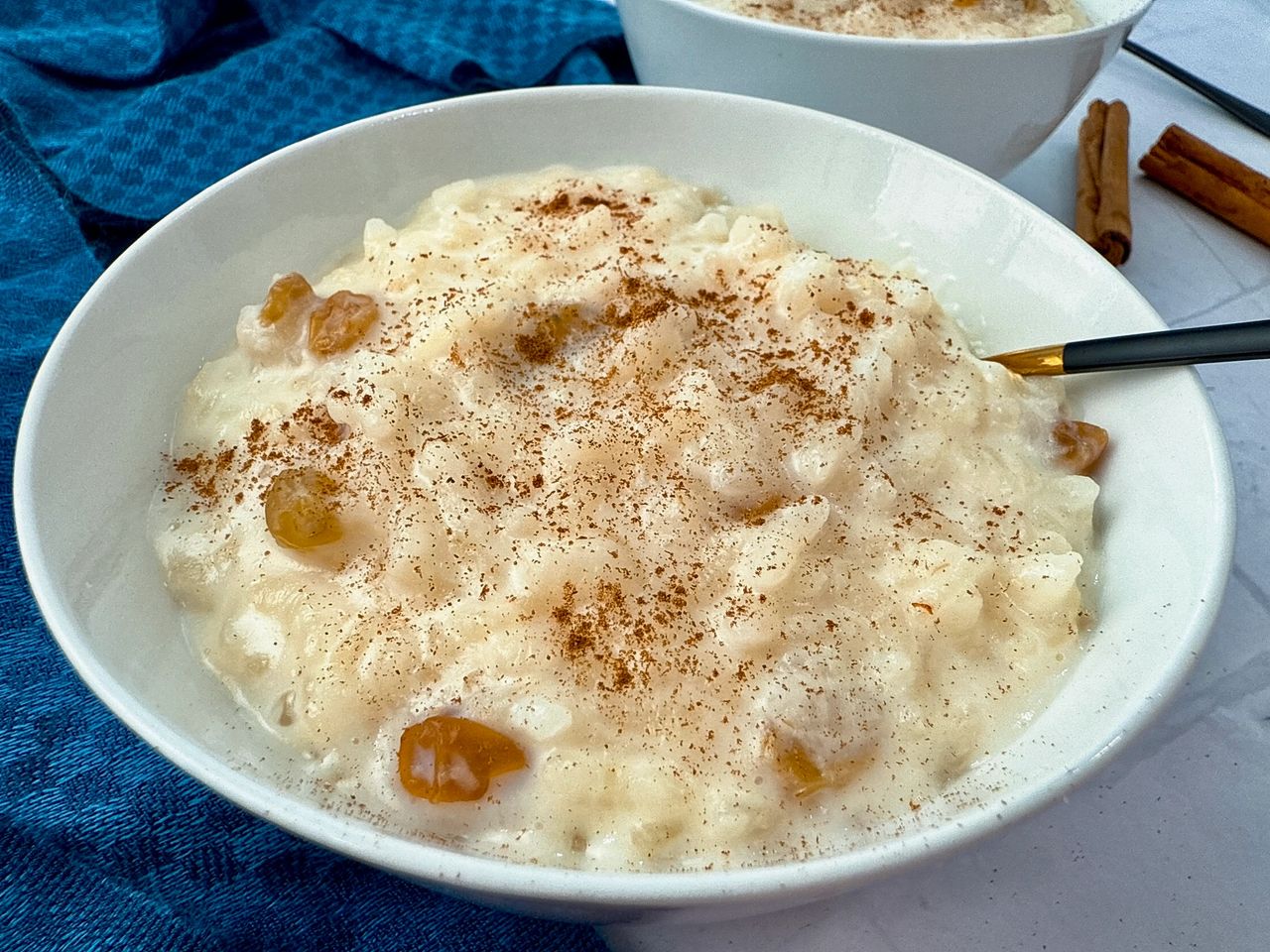 rice pudding in a white bowl with a black spoon and cinnamon sticks on the side