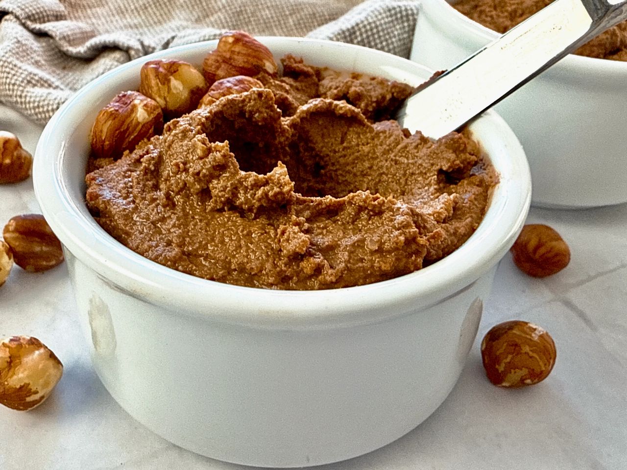 Homemade Chocolate Hazelnut Spread hazelnut spread in a white ramekin with a butter knife