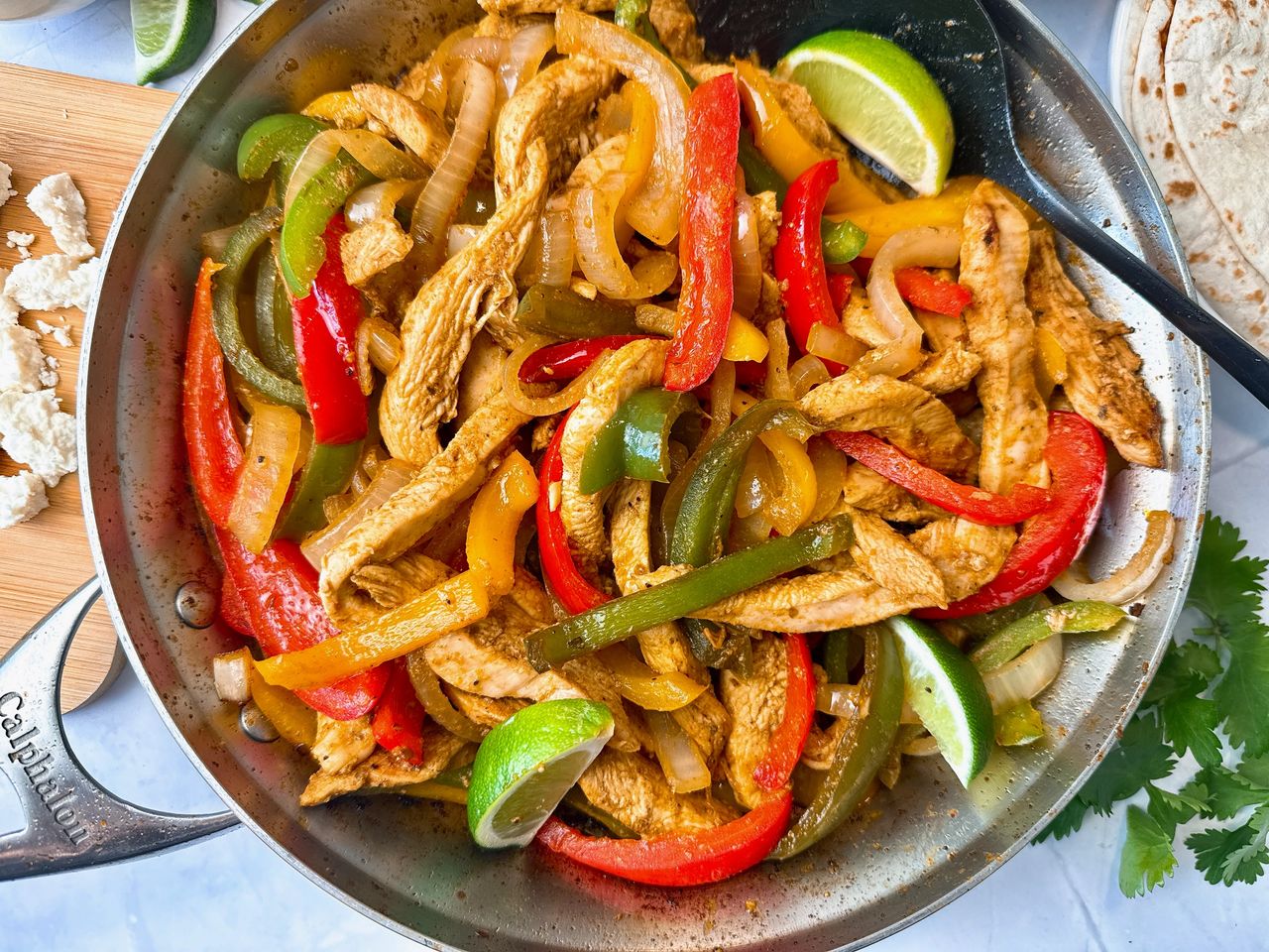 chicken and bell peppers in a skillet with tortillas on the side