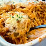 baked spaghetti in a baking dish with a black spoon