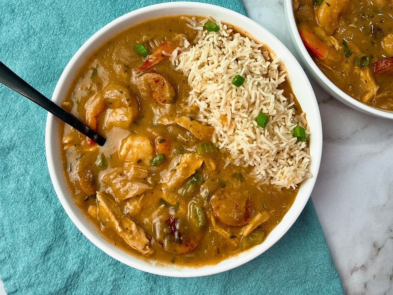 Cajun gumbo and rice in a white bowl with a black spoon