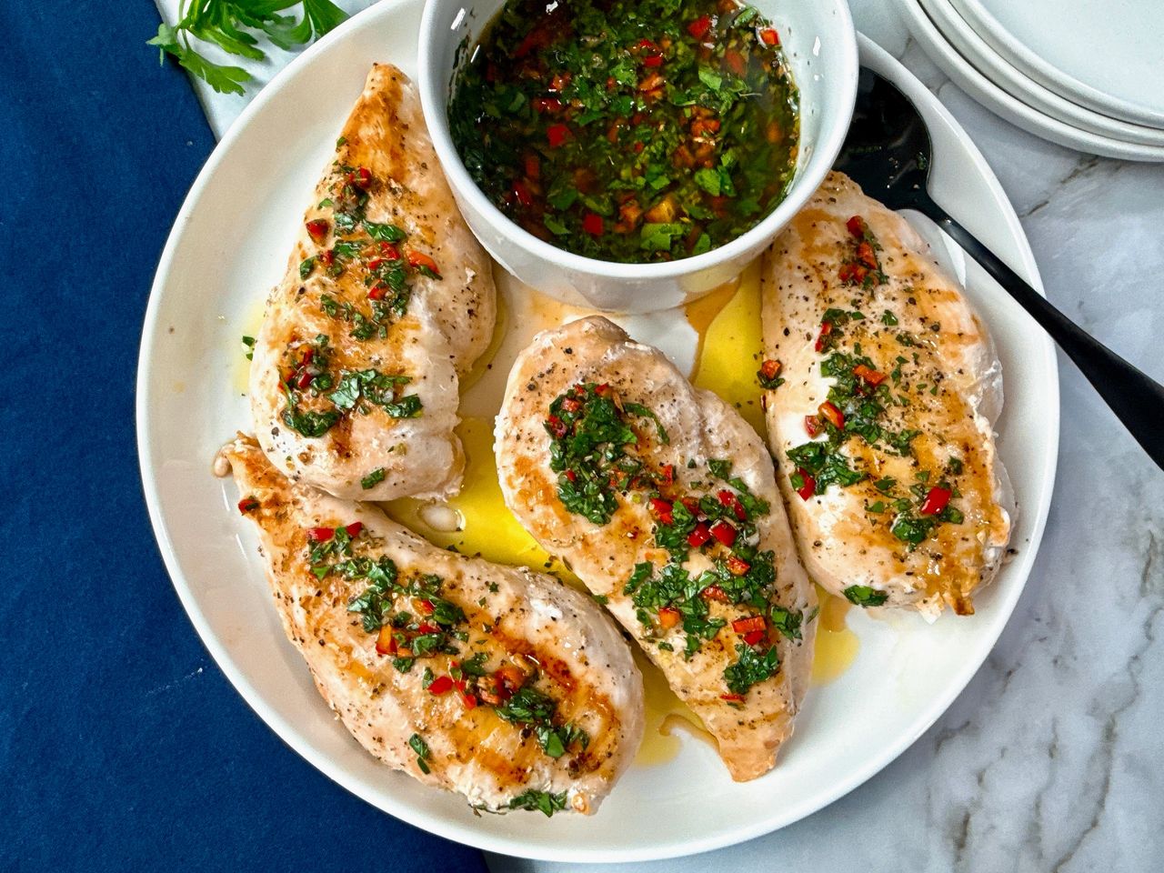 grilled chicken and bowl of chimichurri sauce on a white plate with a black spoon