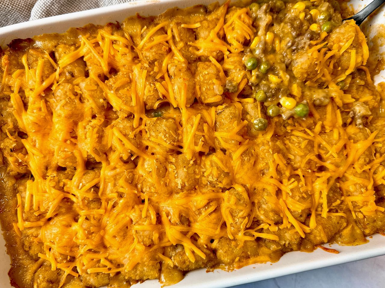 tater tot casserole in a white baking dish and on a spoon
