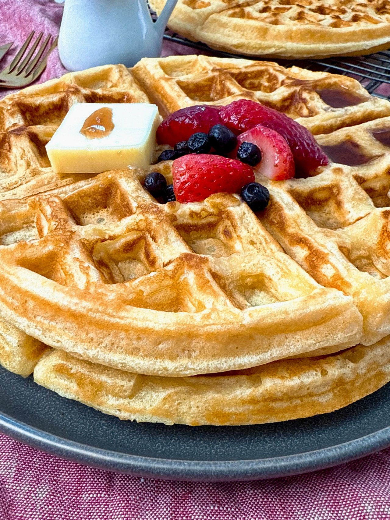 waffles on a grey plate with berries and butter