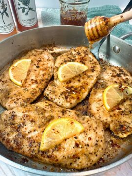 chicken and lemon in a skillet with a drizzle of honey