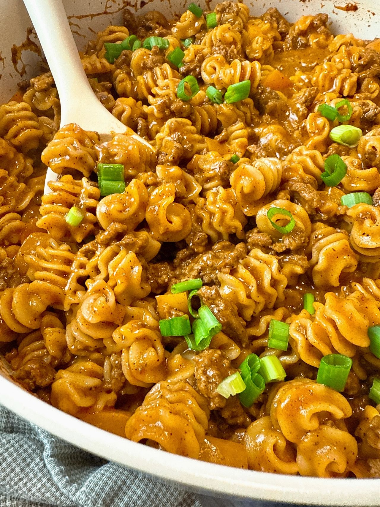 beef and pasta in an enchilada sauce in a white pan with a white spoon