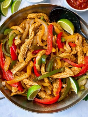 chicken and bell peppers in a skillet with tortillas on the side