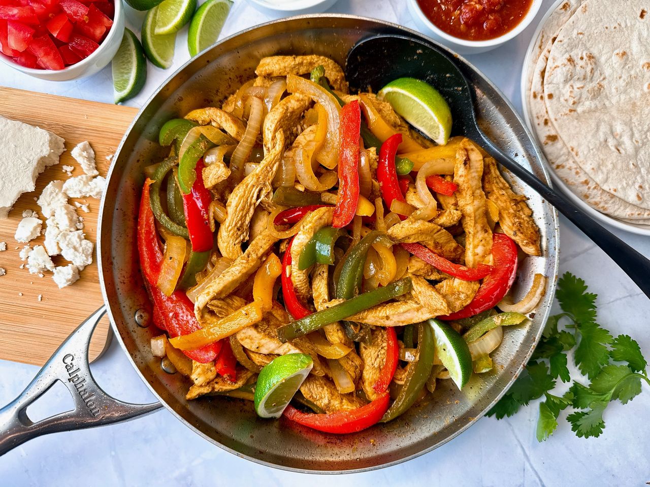 Chicken Fajitas chicken and bell peppers in a skillet with tortillas on the side