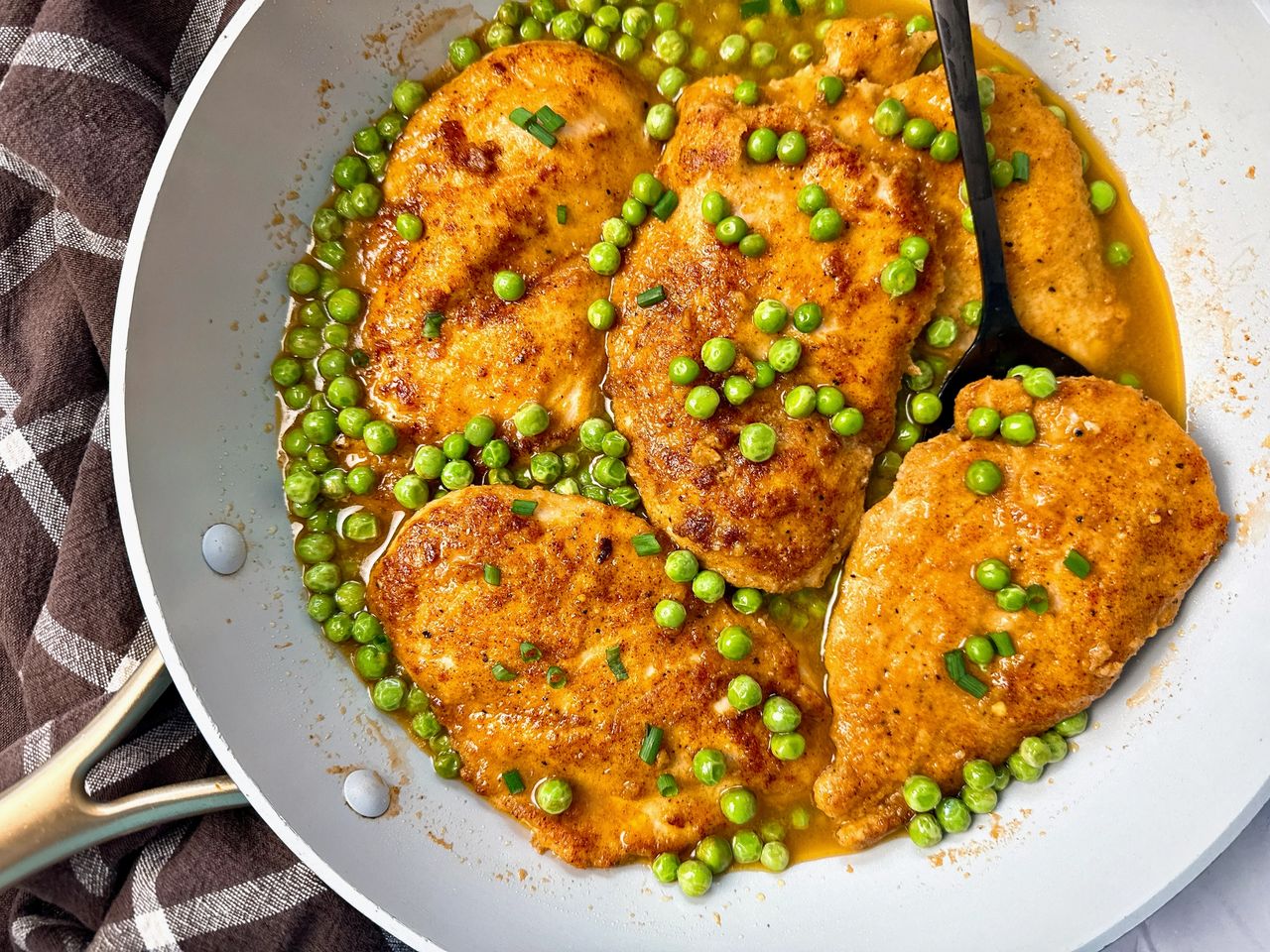 parmesan chicken and peas in wine sauce in white skillet