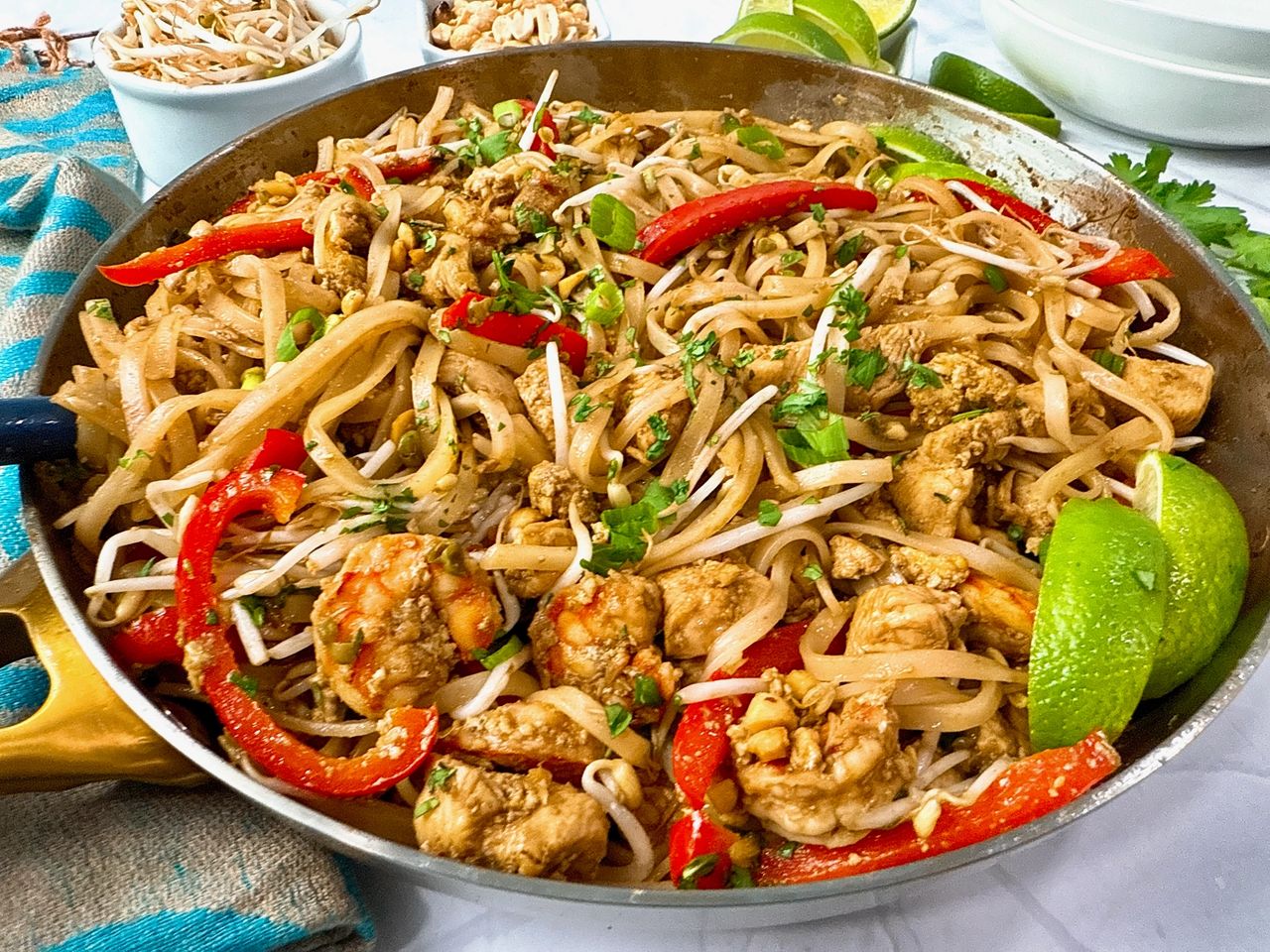 pad thai in a silver skillet with peanuts on the side