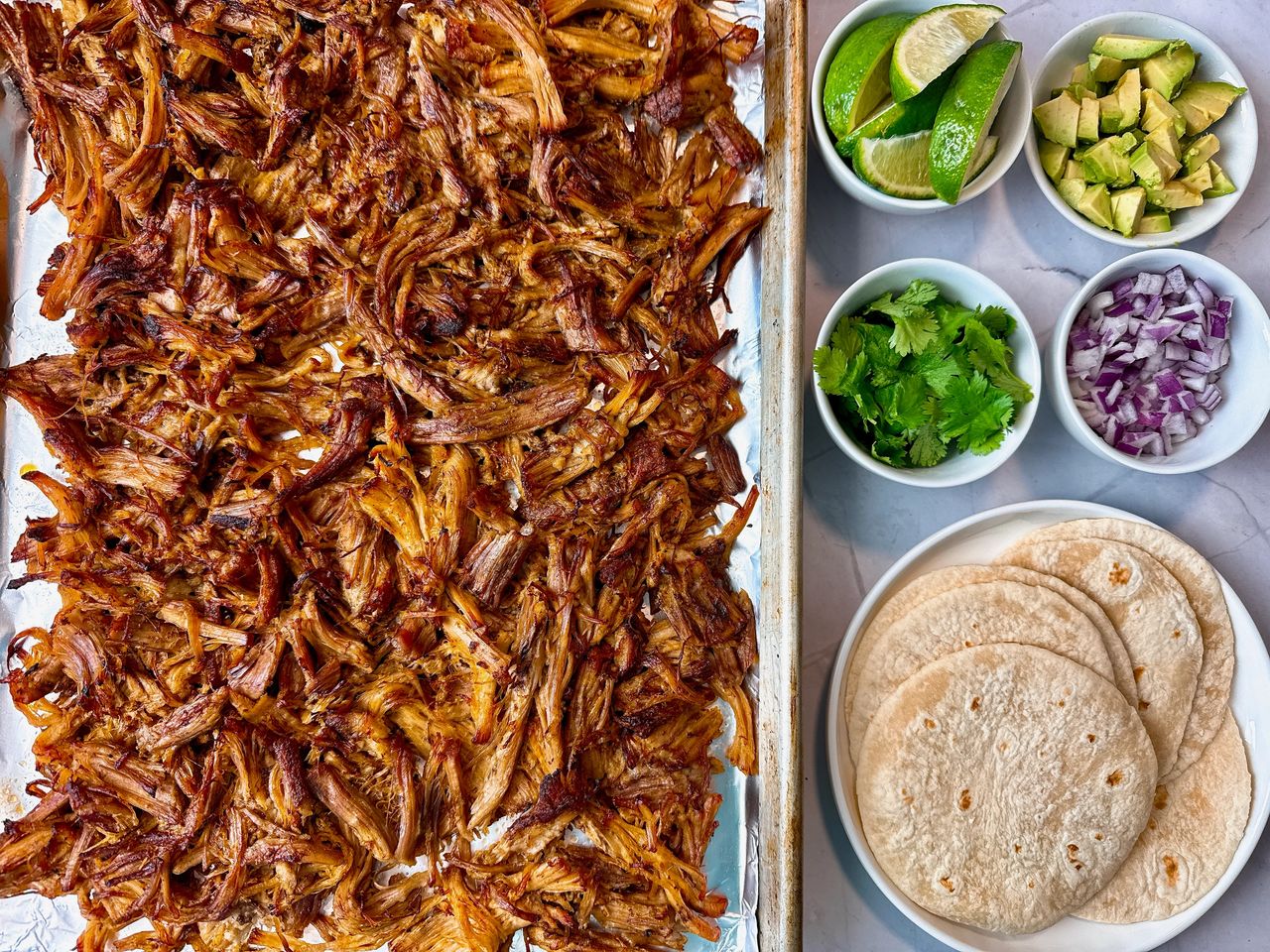 Pork carnitas on a sheet pan with garnishes on the side