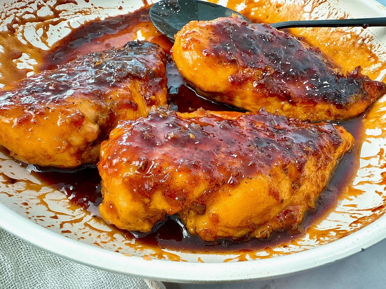 hot honey chicken in a white skillet with a black spoon