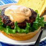 burger on a bun with lettuce and spicy sauce