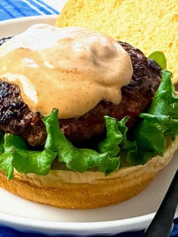 burger on a bun with lettuce and spicy sauce
