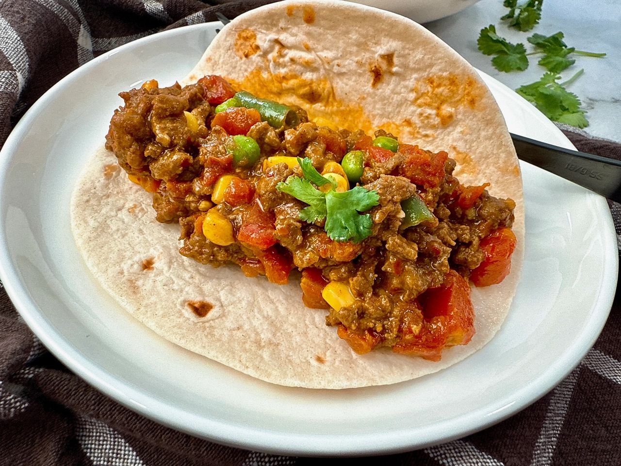 ground beef and vegetables in a tortilla on a white plate