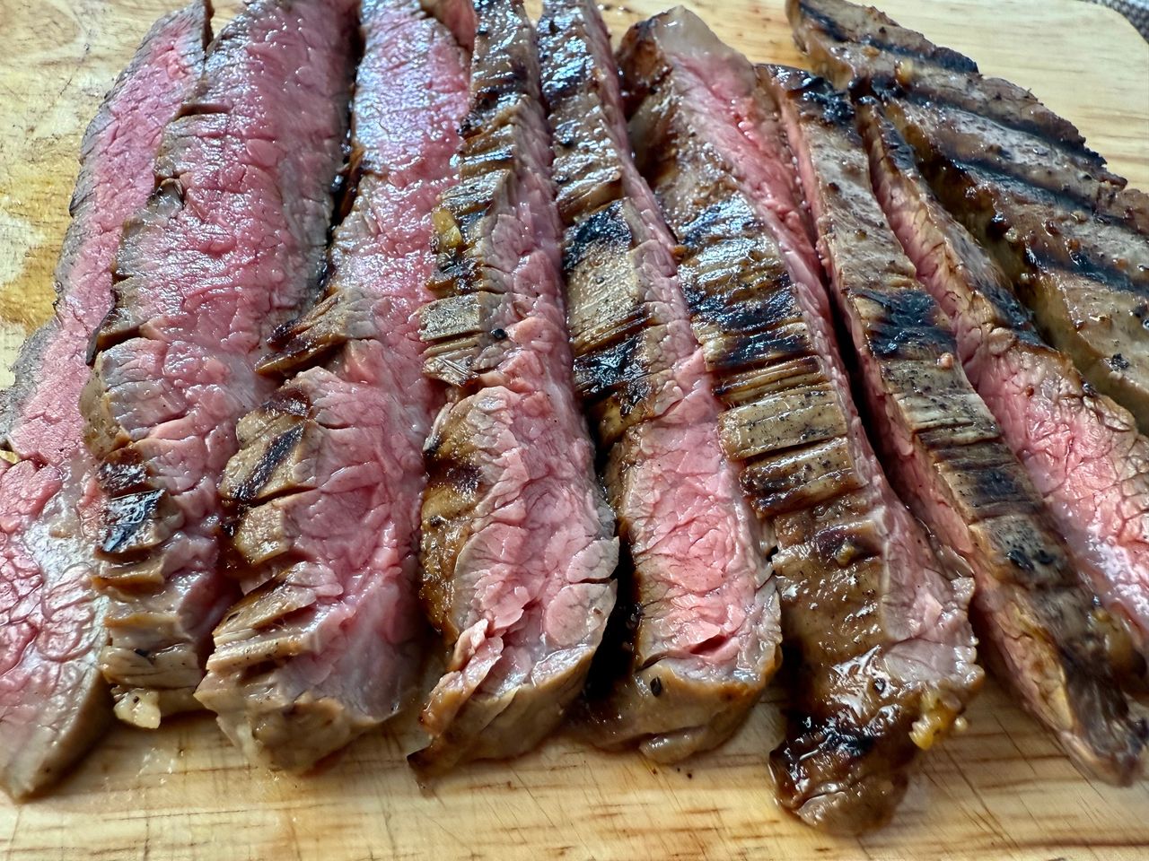 grilled flank steak slices on a wooden cutting board