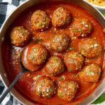 meatballs and marinara sauce in a pan with a black serving spoon