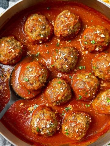meatballs and marinara sauce in a pan with a black serving spoon