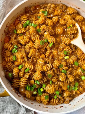beef and pasta in an enchilada sauce in a white pan with a white spoon