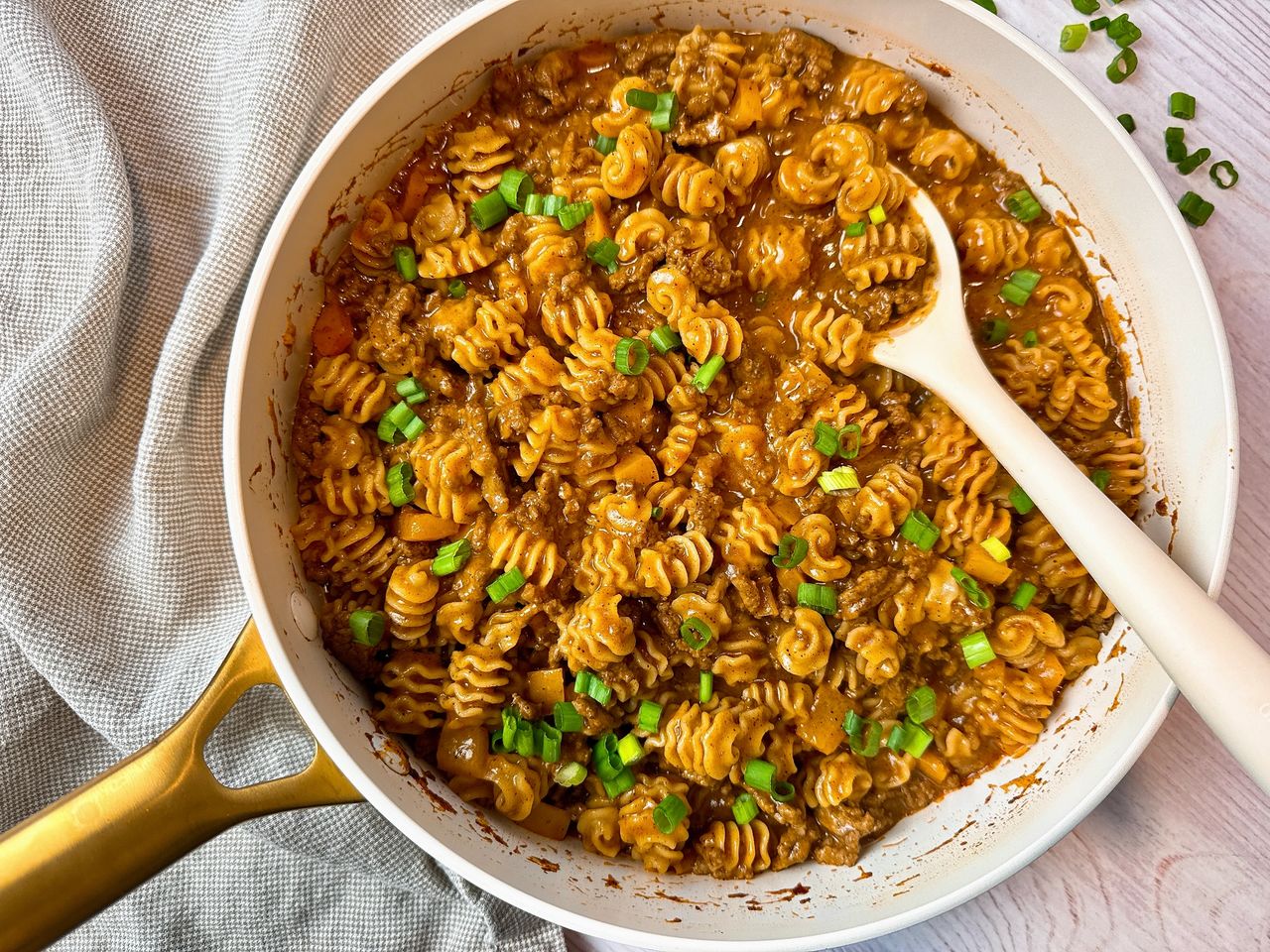 beef and pasta in an enchilada sauce in a white pan with a white spoon