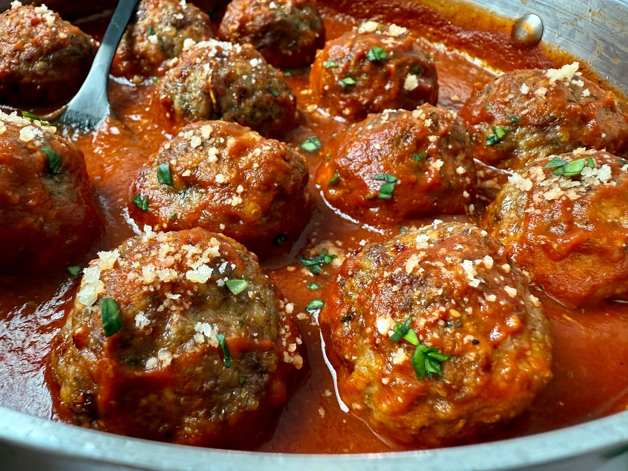 meatballs and marinara sauce in a pan with a black serving spoon