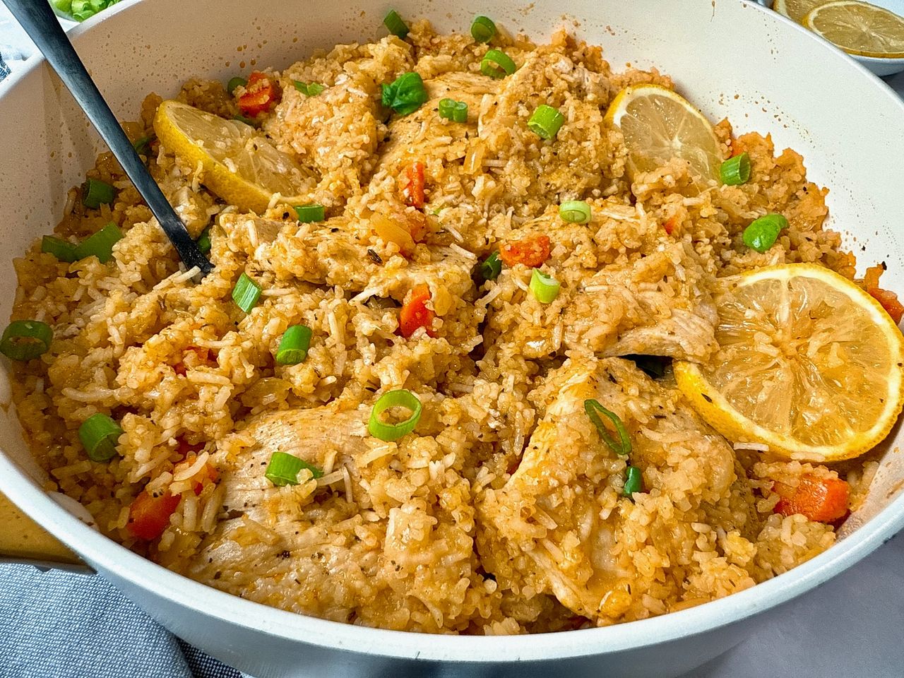 chicken and rice in a white saucepan with lemon garnish