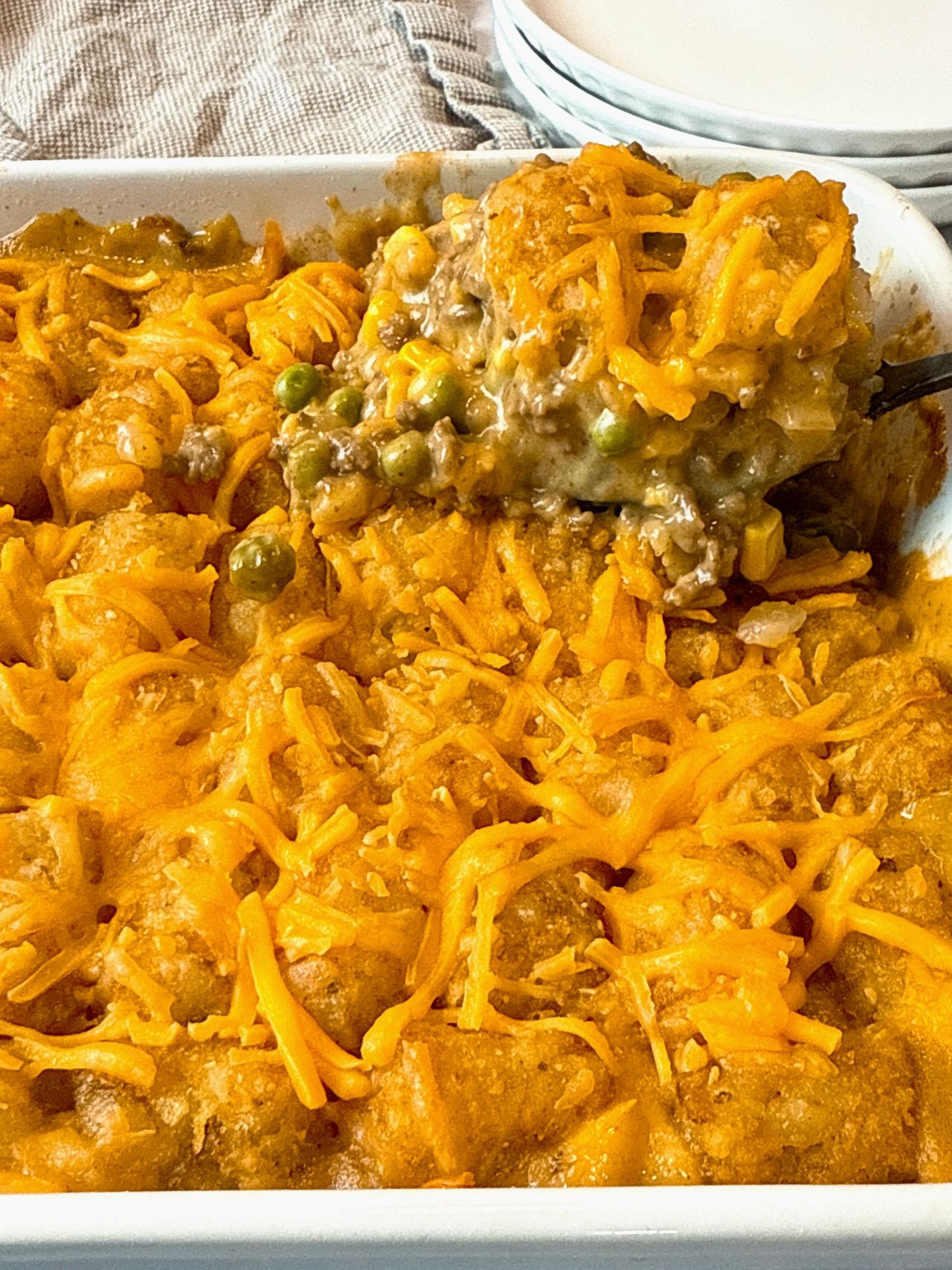 tater tot casserole in a white baking dish and on a spoon