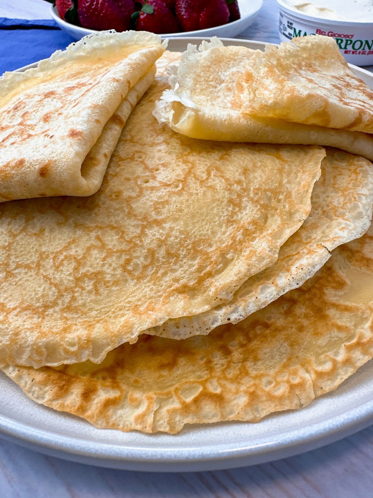 Crepes stacked on a plate with mascarpone cheese and served with strawberries