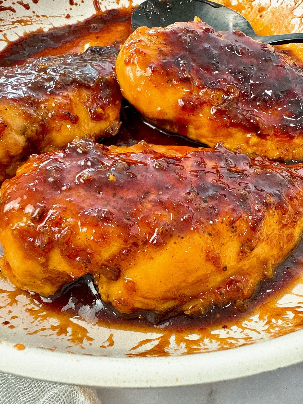 hot honey chicken in a white skillet with a black spoon
