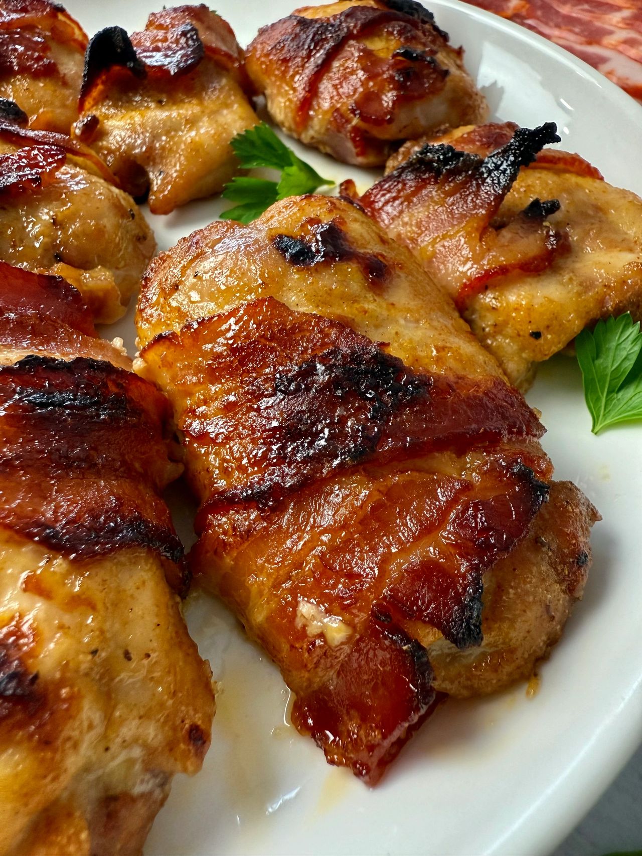 bacon wrapped chicken on a white plate with parsley garnish