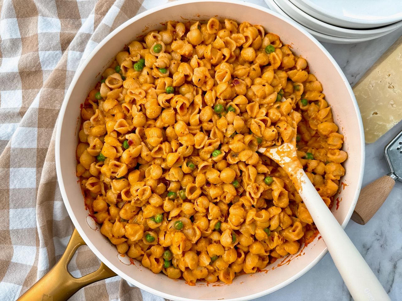 Creamy Pasta and Peas in a white saucepan with a white spoon and cheese on the side