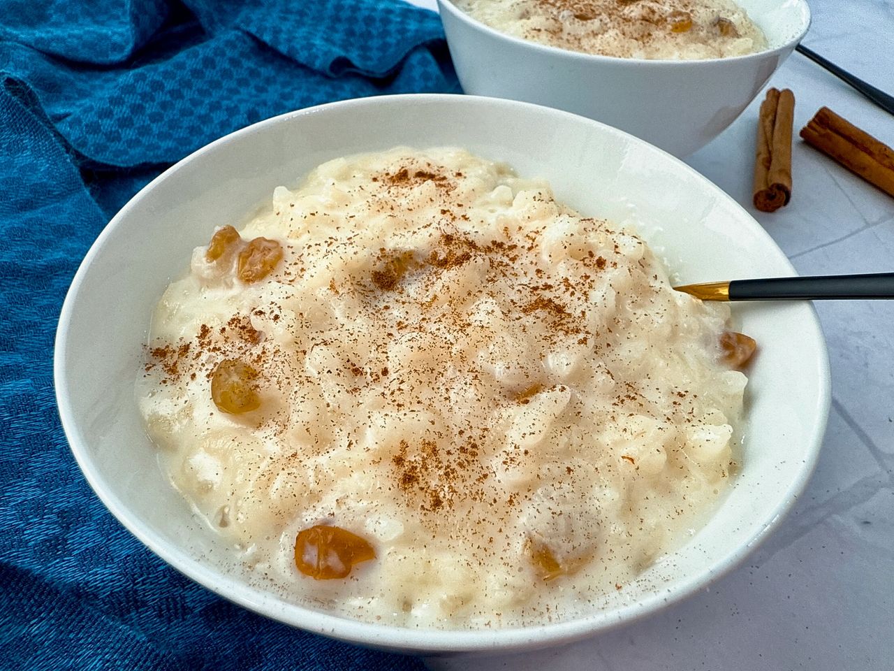 rice pudding in a white bowl with a black spoon and cinnamon sticks on the side