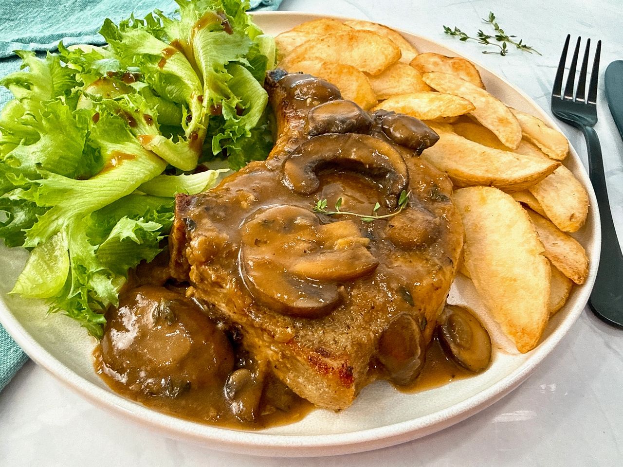 Pork Chops with Mushroom Gravy on a white plate with potato wedges and a green salad