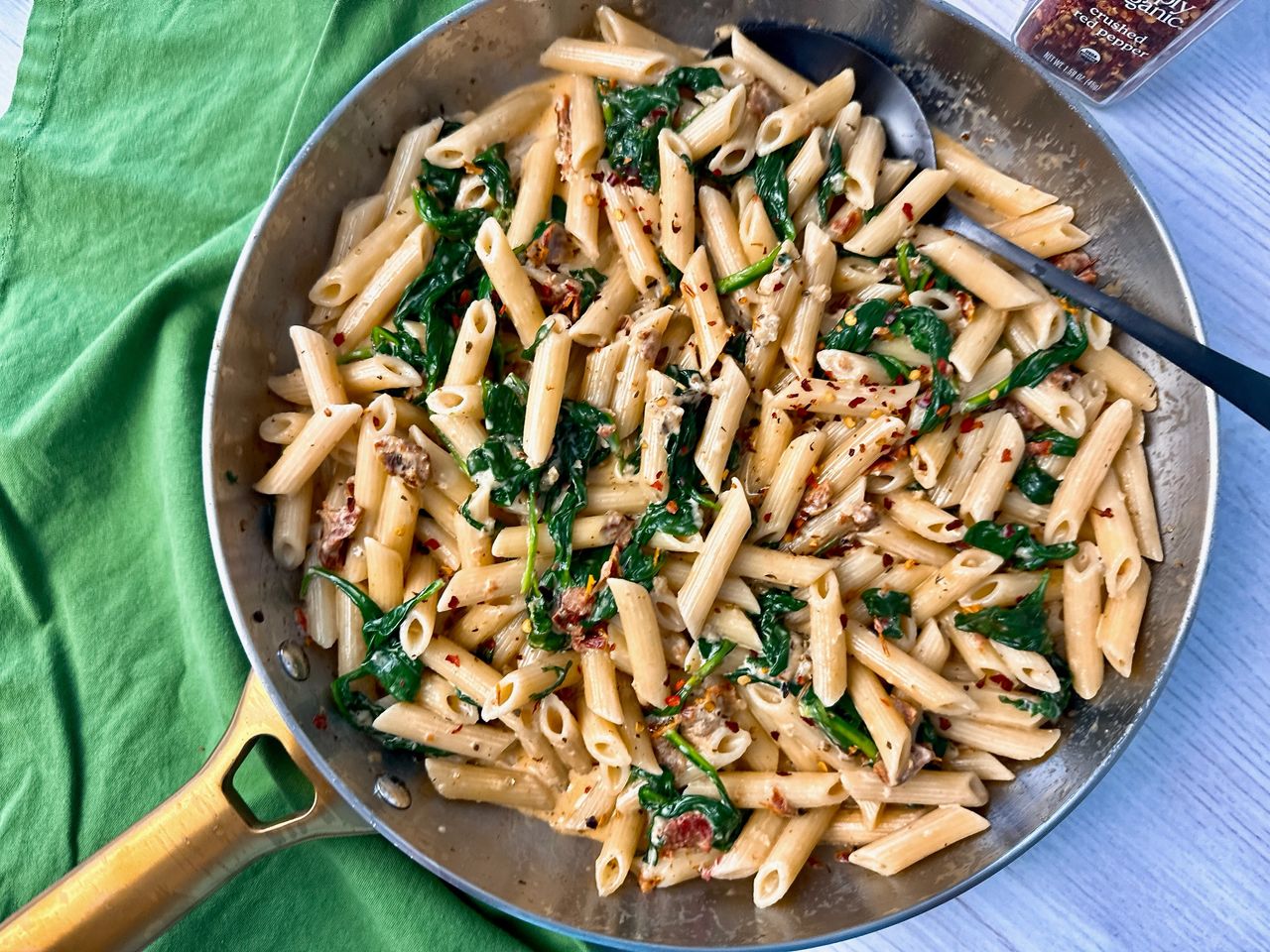 penne pasta, spinach, and sun dried tomatoes in a skillet 