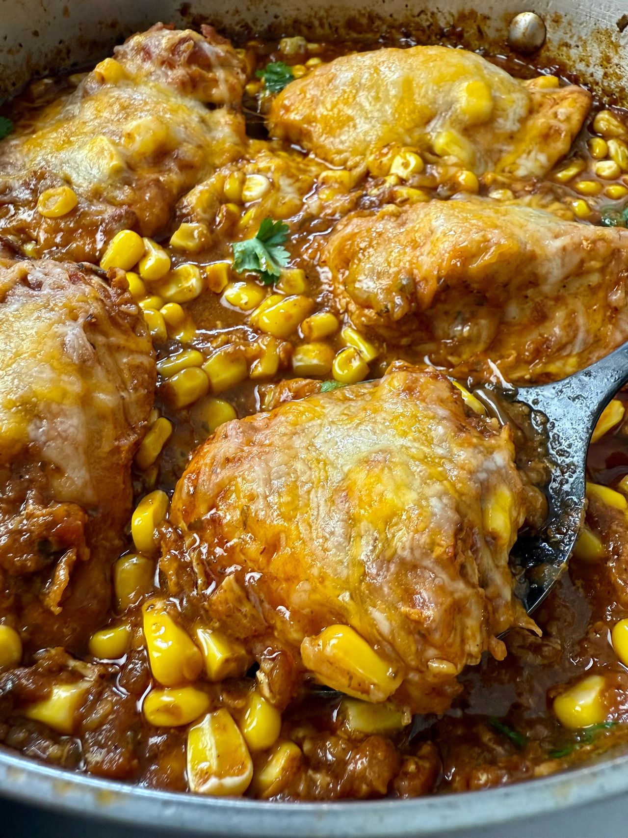 salsa chicken with cheese in a silver pan with a black spoon