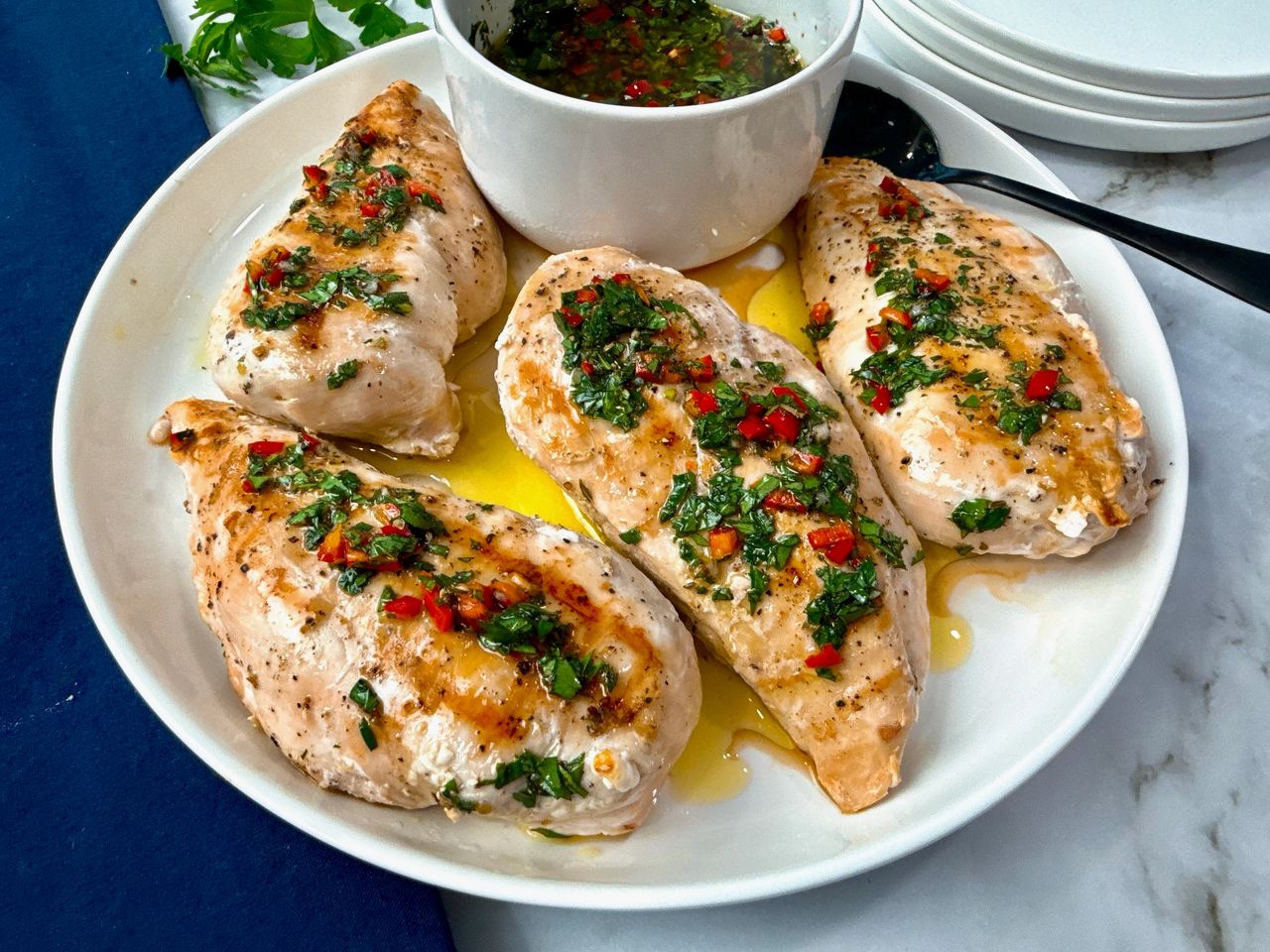 grilled chicken and bowl of chimichurri sauce on a white plate with a black spoon