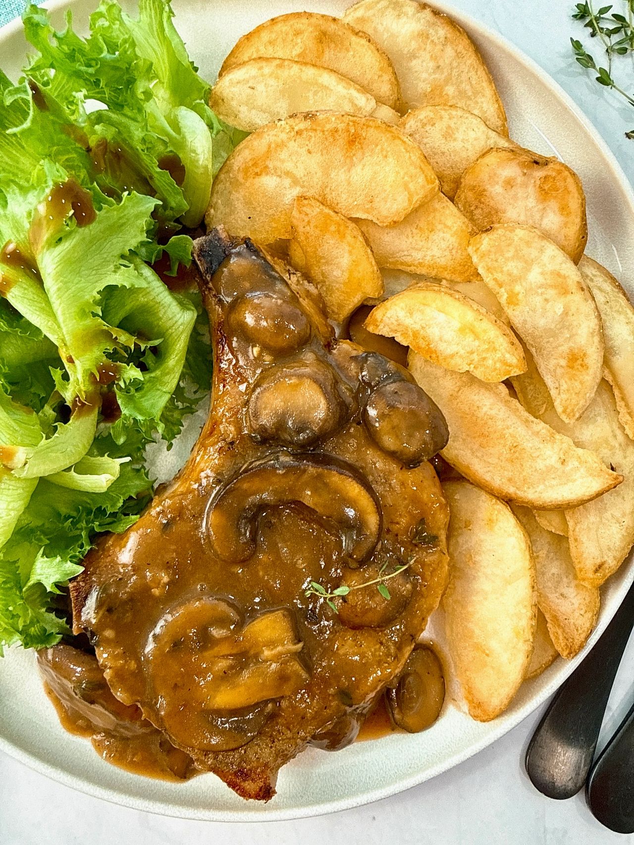 Pork Chops with Mushroom Gravy on a white plate with potato wedges and a green salad
