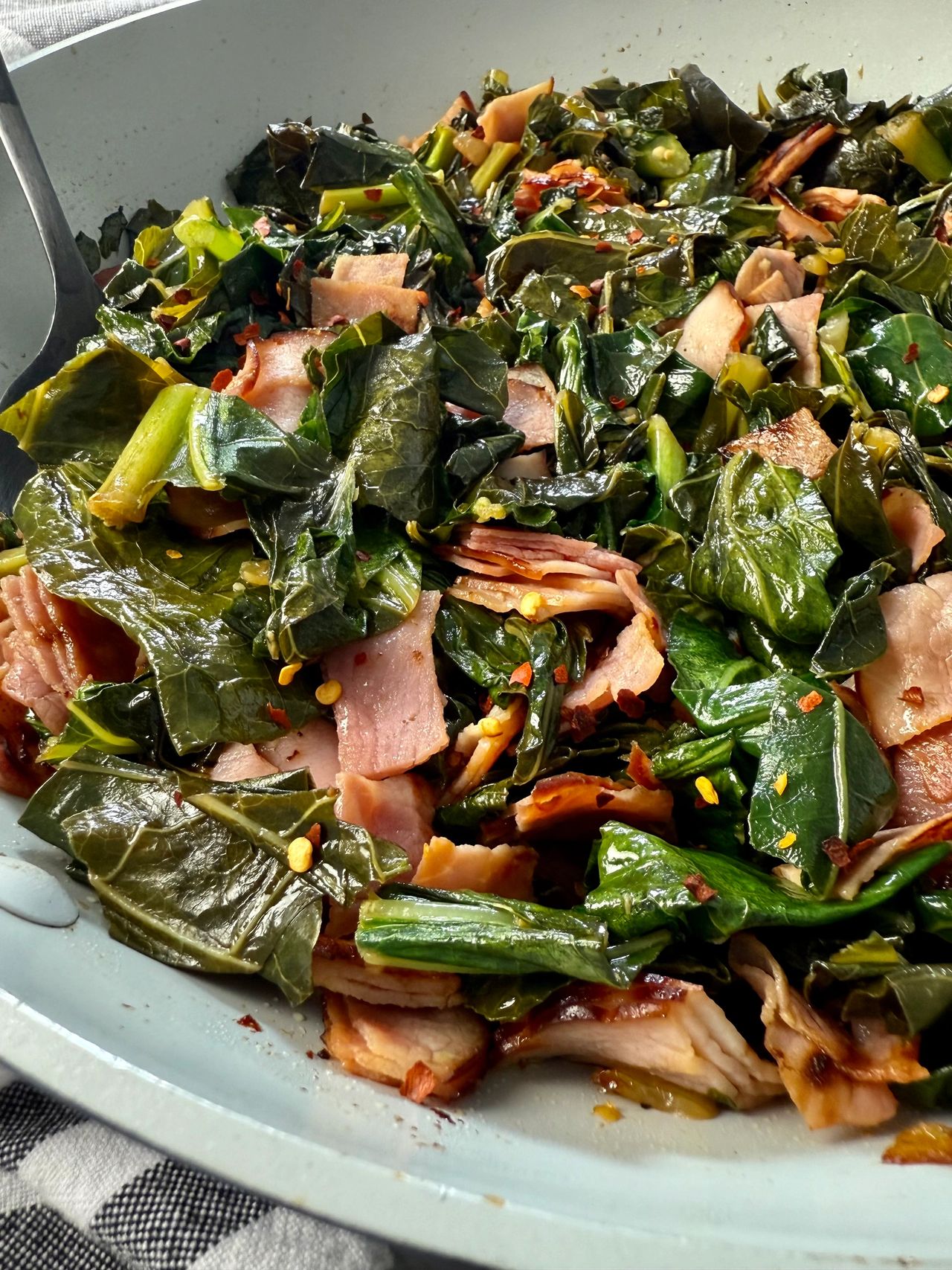 collard greens and ham in a white skillet