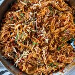 pasta bolognese in a silver pan with a black spoon