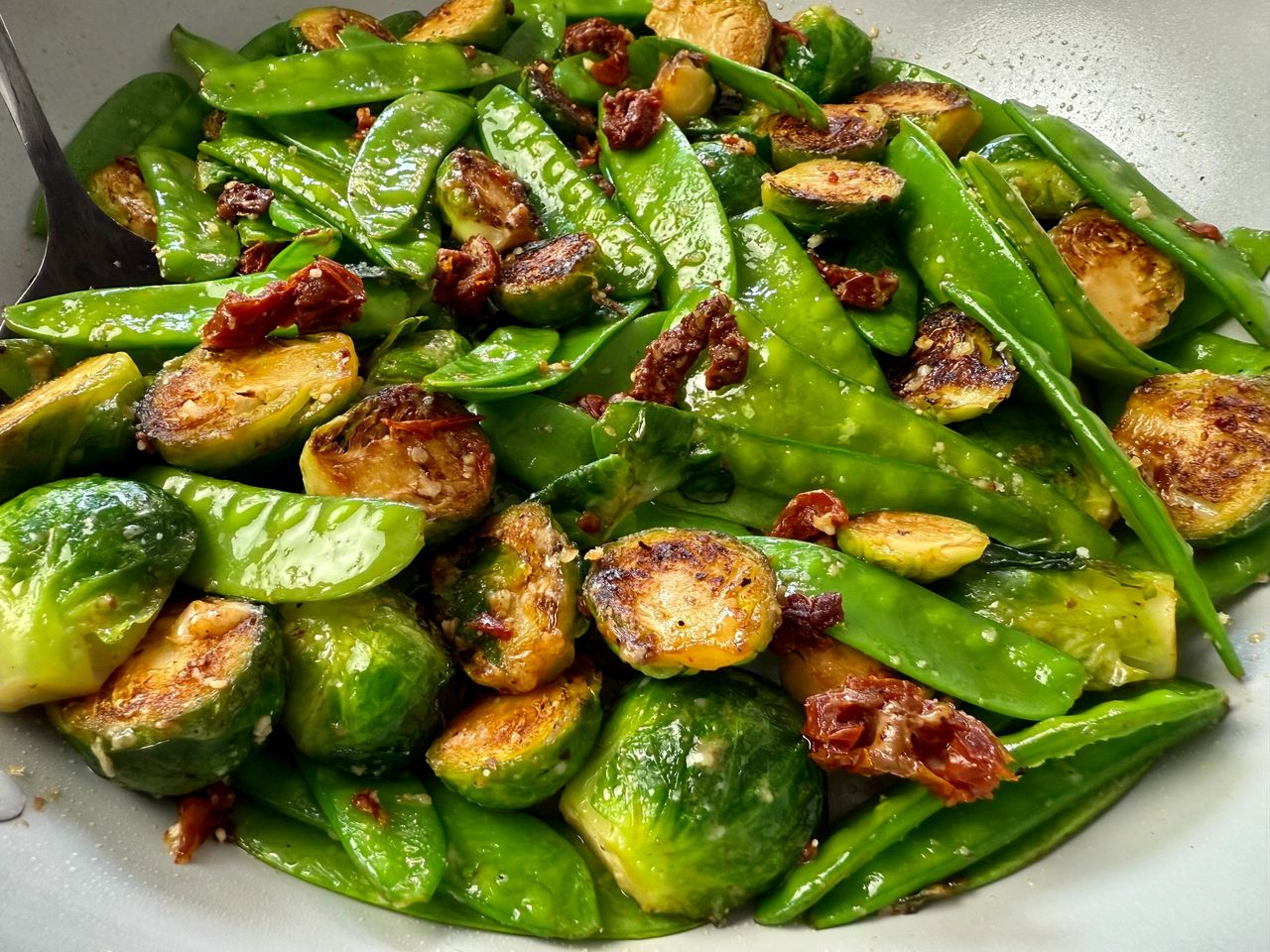 brussels sprouts, snow peas, and sun dried tomatoes in a white skillet