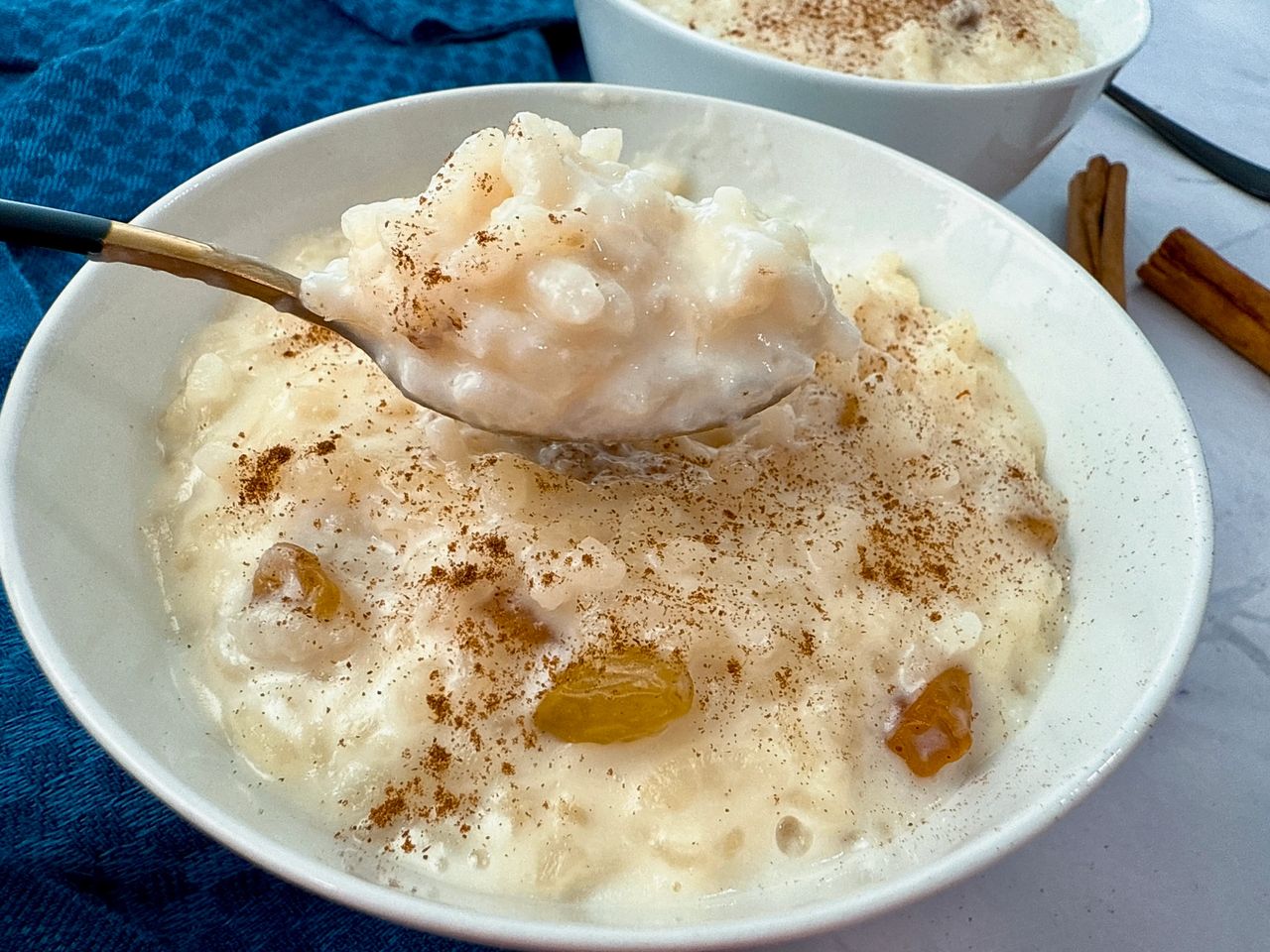 rice pudding in a white bowl with a black spoon and cinnamon sticks on the side
