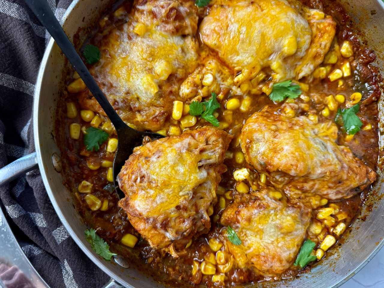 salsa chicken with cheese in a silver pan with a black spoon