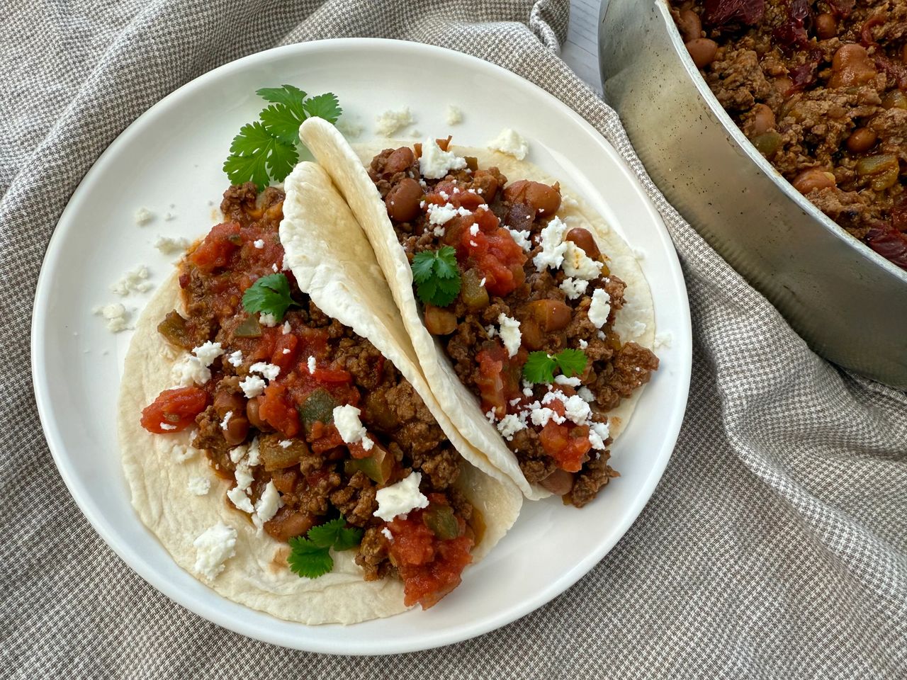 ground beef and bean soft tacos on a white plate with crumbled cheese garnish