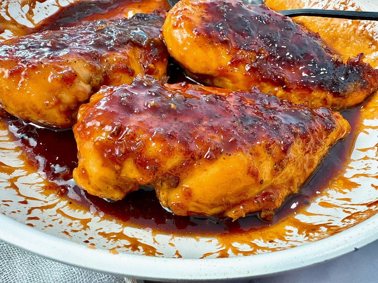 hot honey chicken in a white skillet with a black spoon