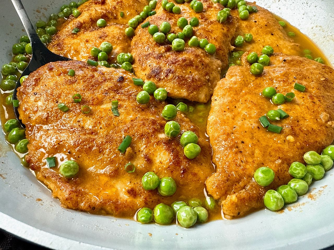 parmesan chicken and peas in wine sauce in white skillet