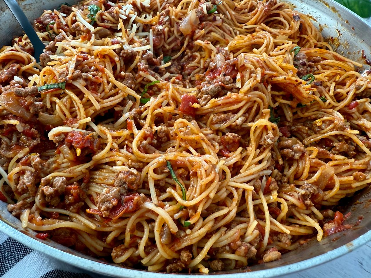 pasta bolognese in a silver pan with a black spoon